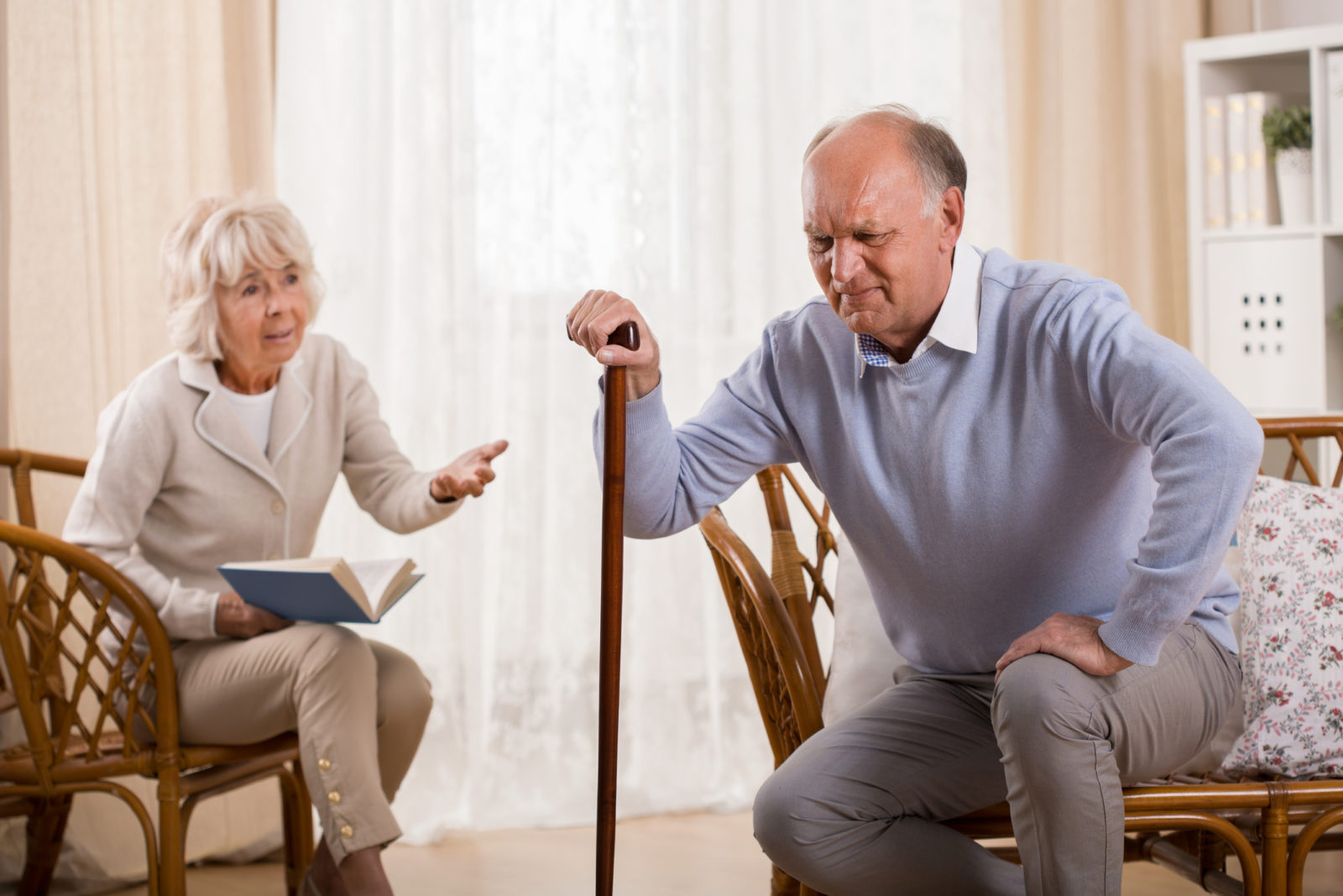 Senior man with knee arthritis trying to get up from chair and caring wife